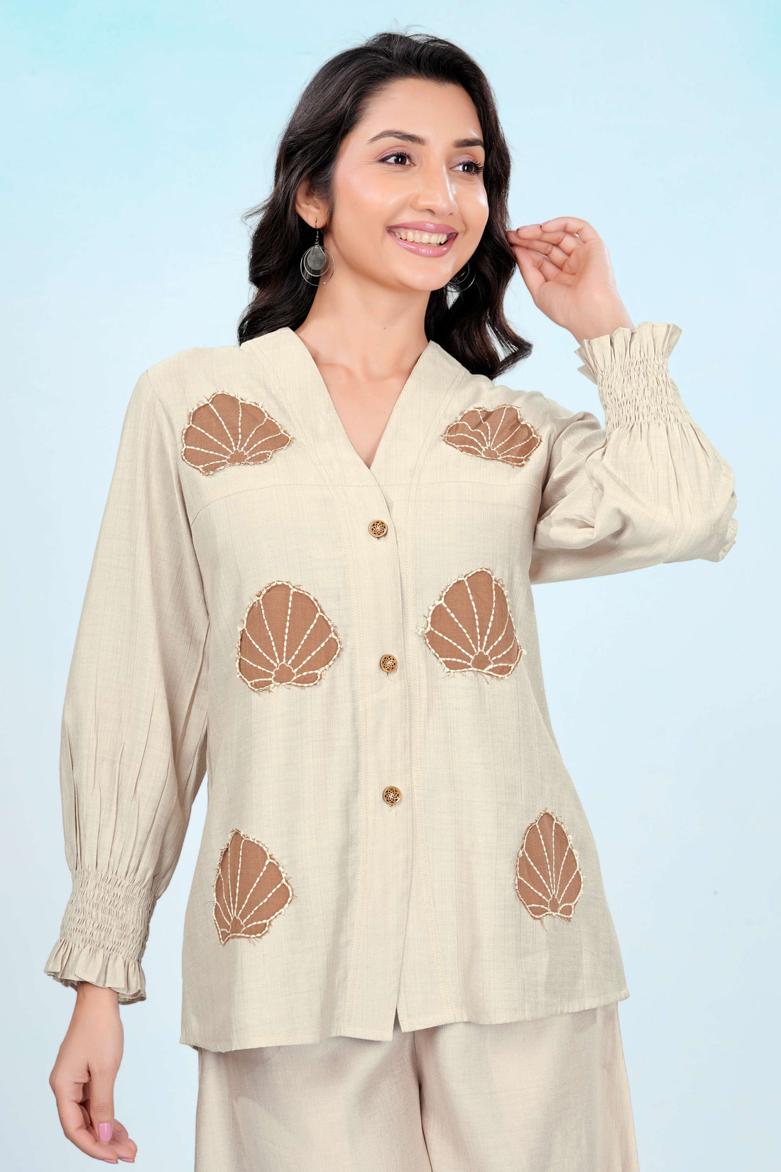 Woman wearing a beige outfit with shell patterns on a light blue background
